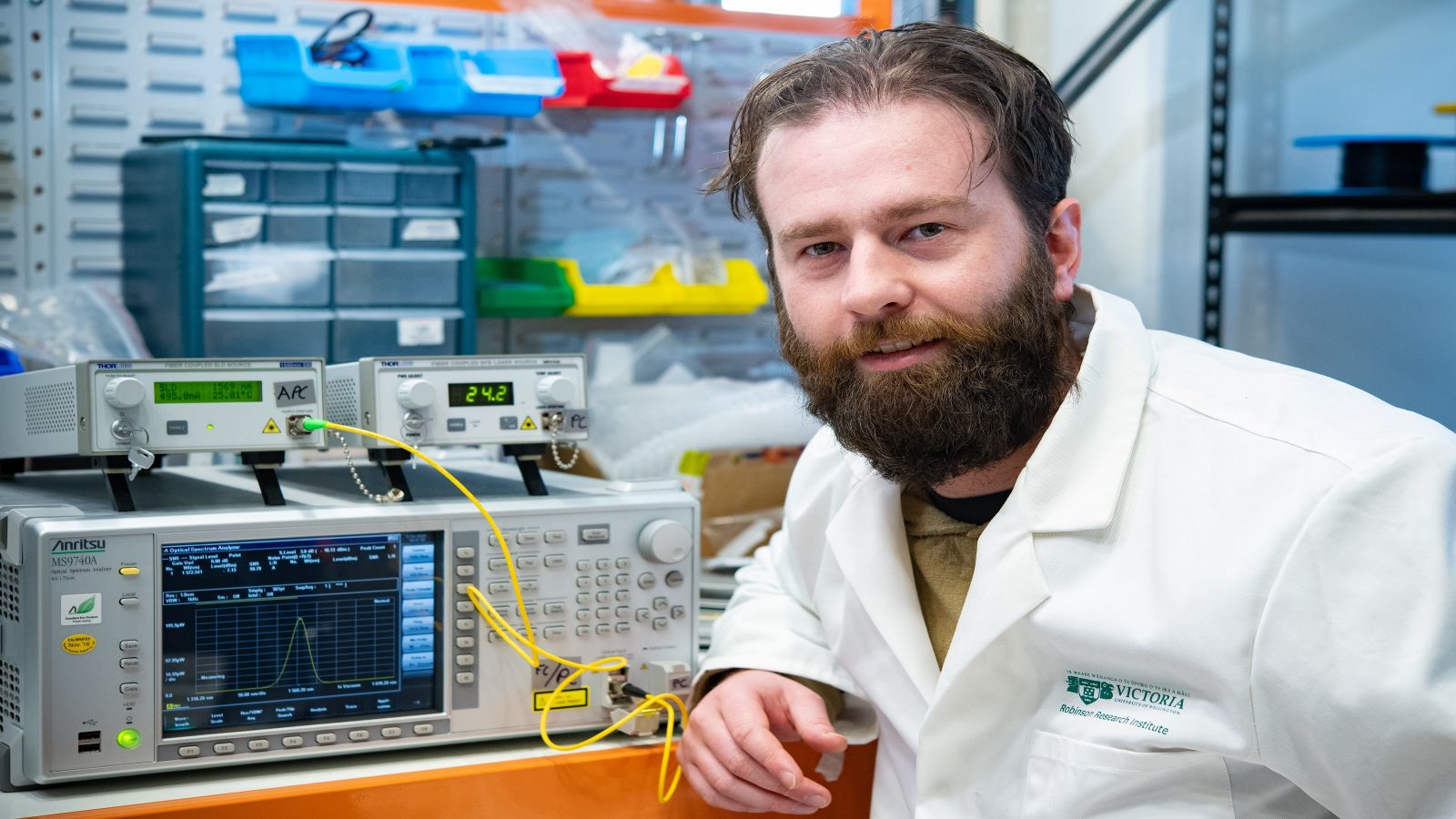 A male researcher sitting in front of lab equipment including an optical spectrum analyser.