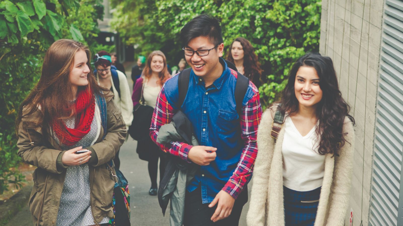 A group of young people, 5 girls and one boy, looking happy, walking to the University.