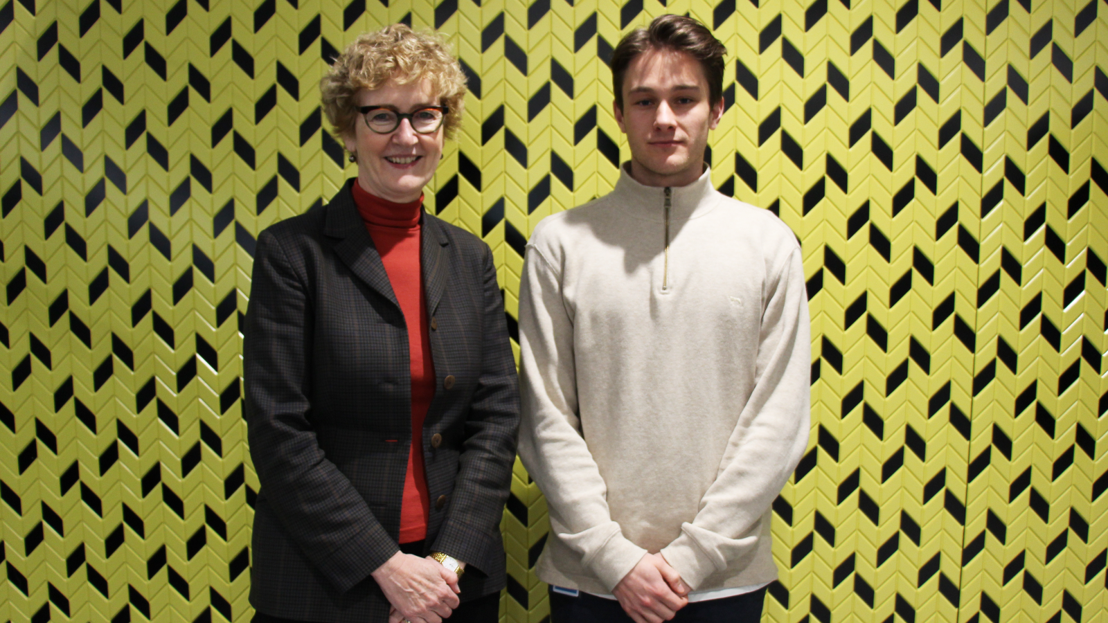 Professor Jane Bryson and Sam Dobbs stand together in front of yellow patterned wall.