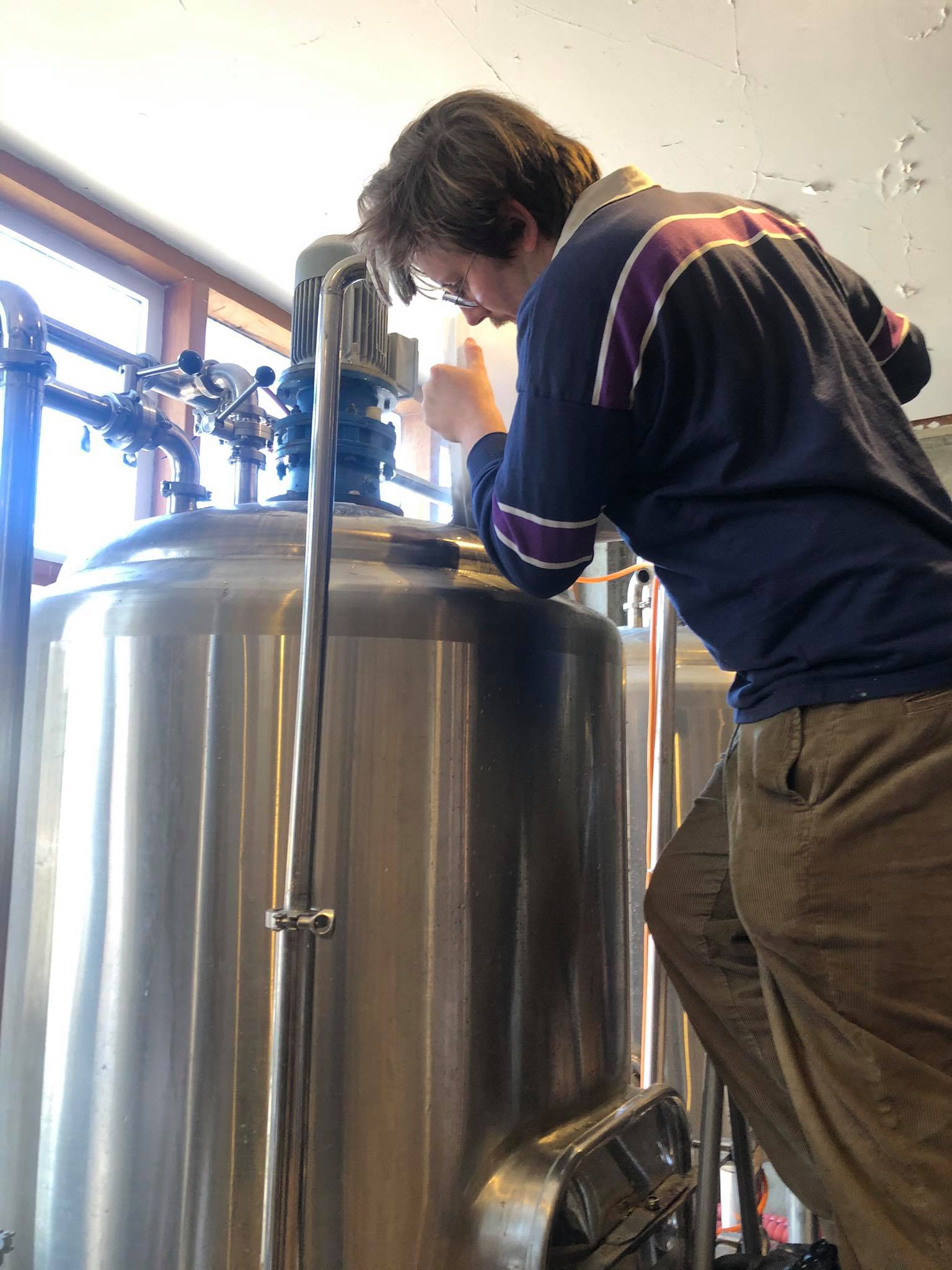 A male pour contents of a bucket into a fermentation vessel for making beer