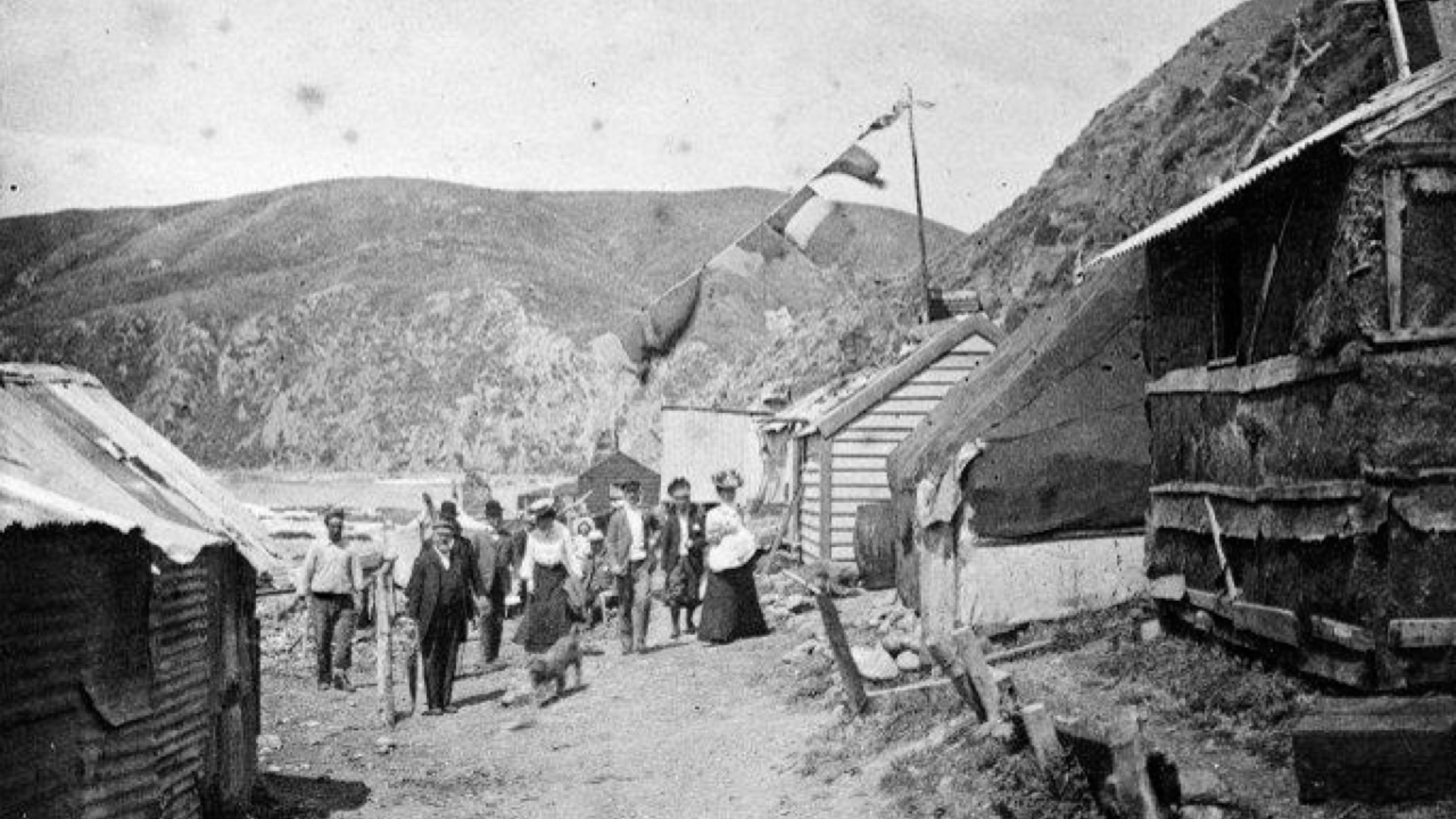 Black and white photo of European settlers next to shacks on a beach