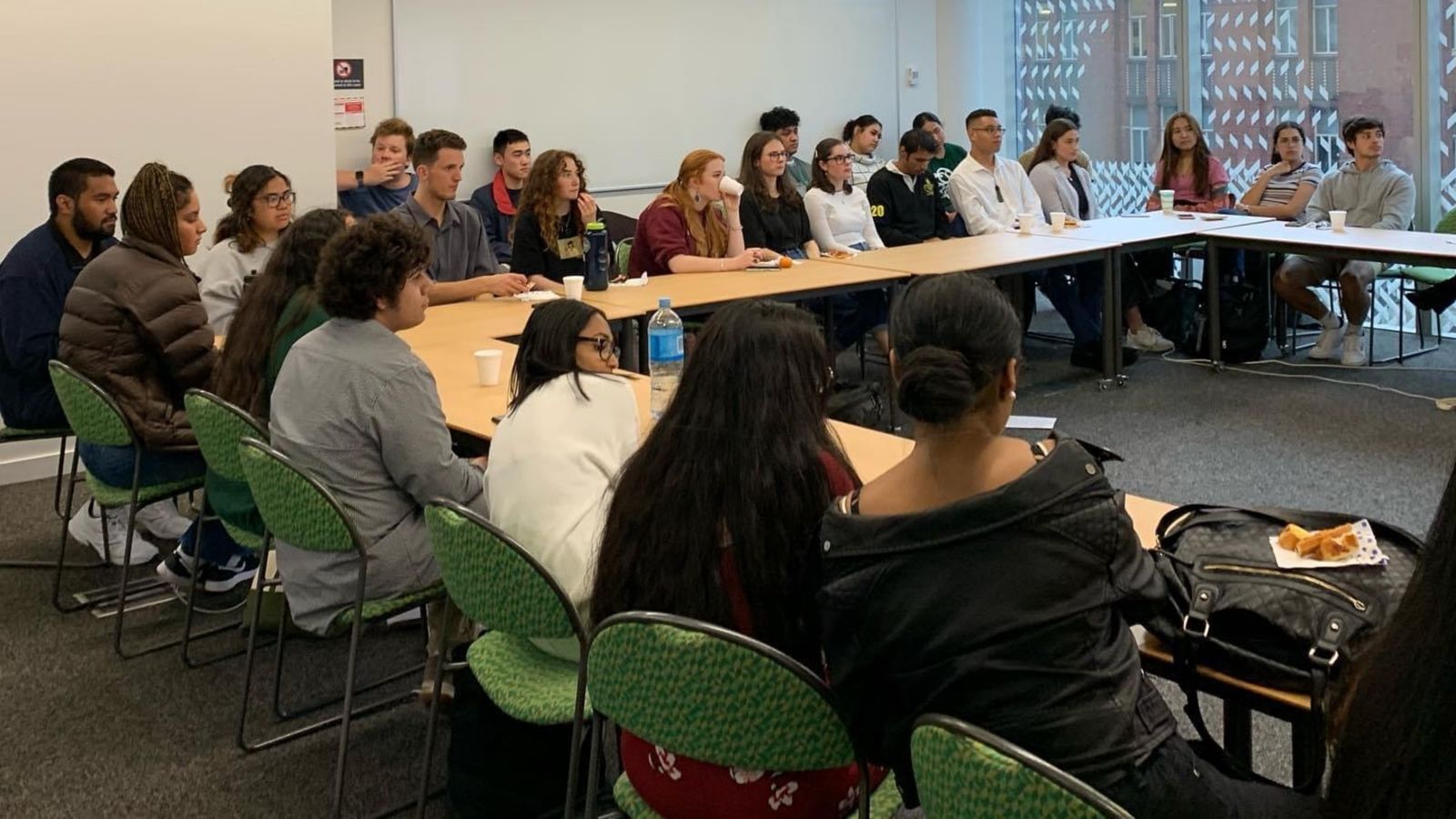Students sitting around tables arranged in square.