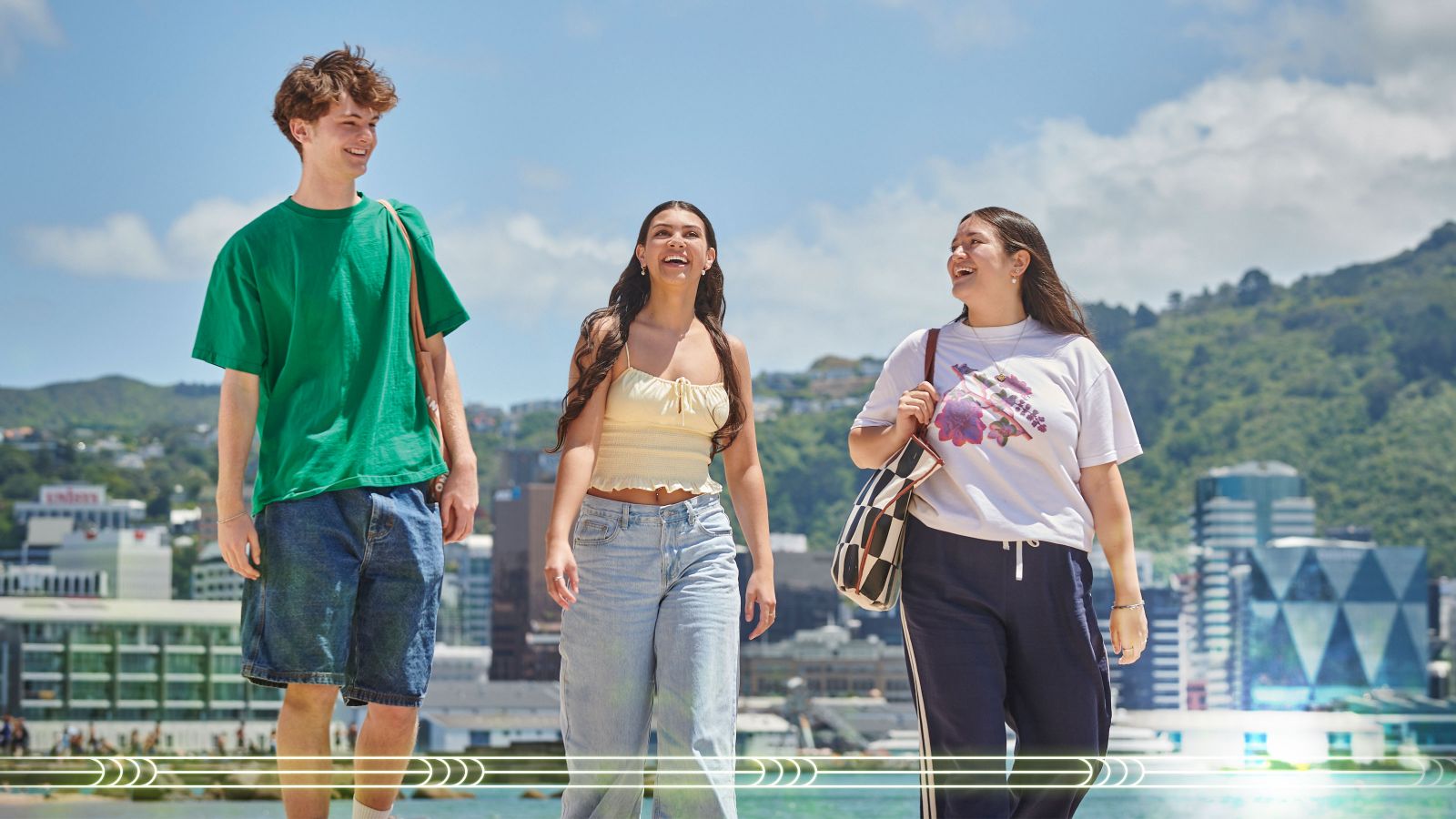 Three students walking along Oriental Bay, with Wellington City in the background.