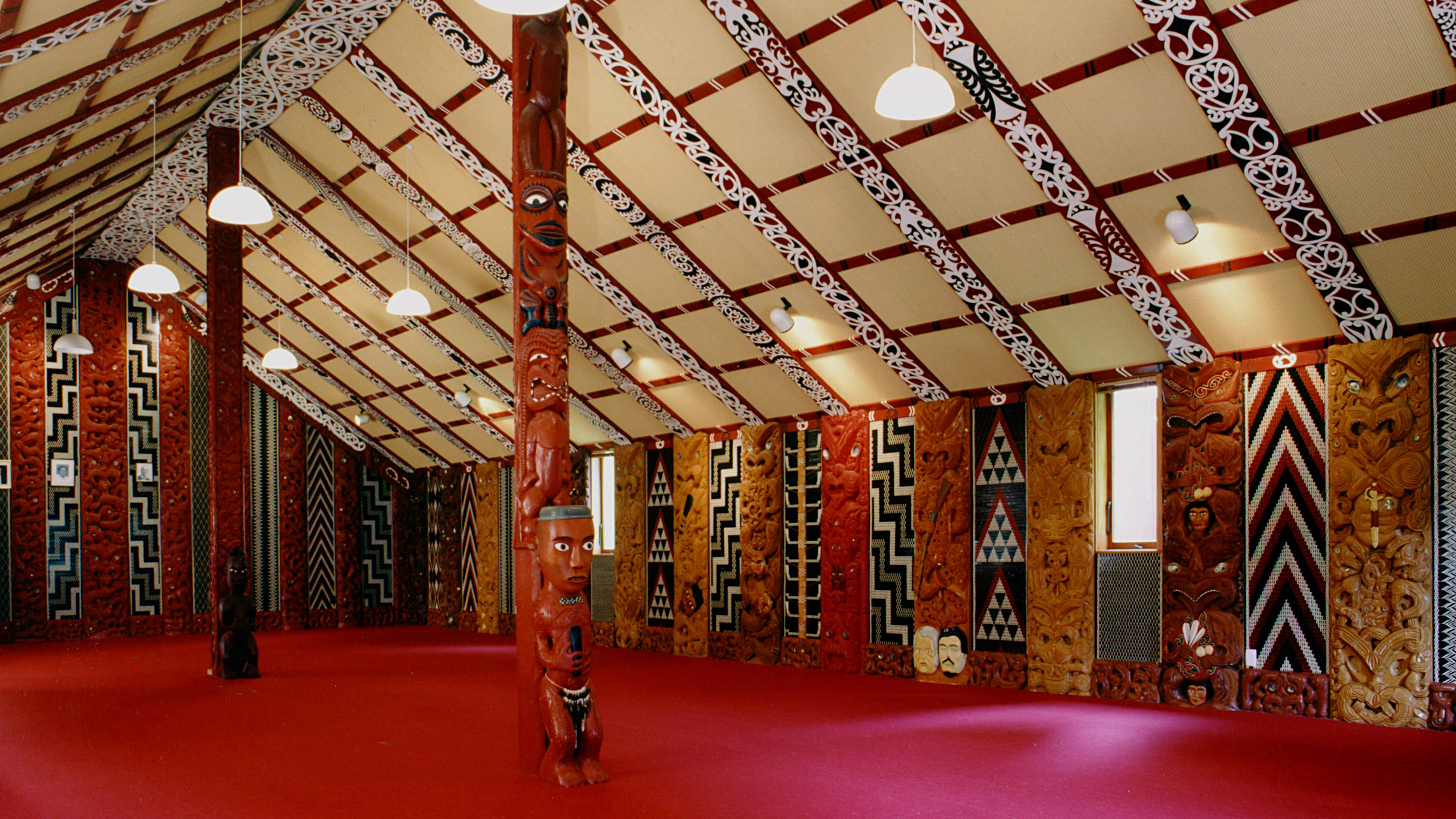 Interior of the whare whakairo with carved posts and woven tukutuku panels