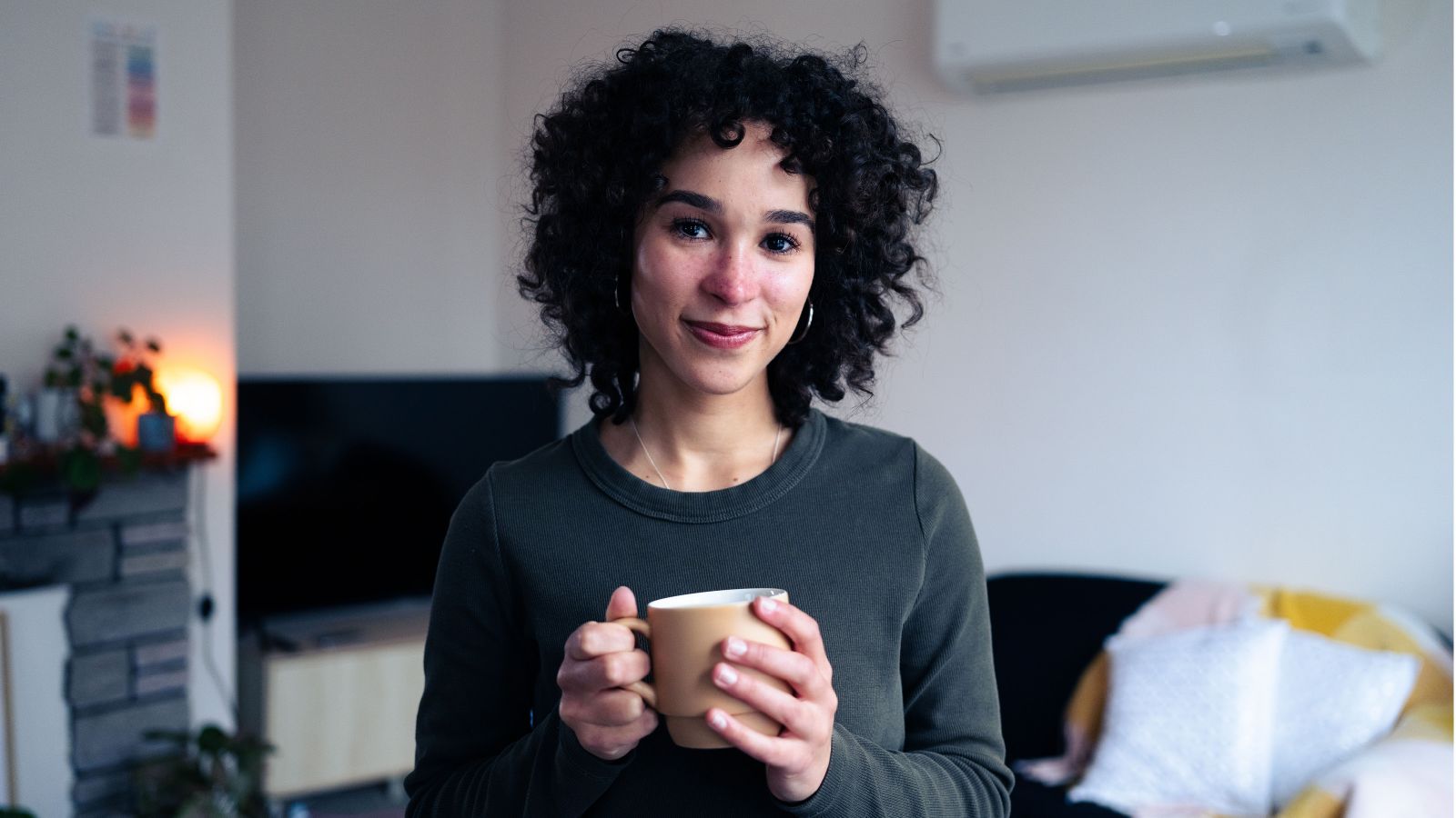 Saraya Rowlands holds a ceramic mug of tea while standing in her flat's lounge