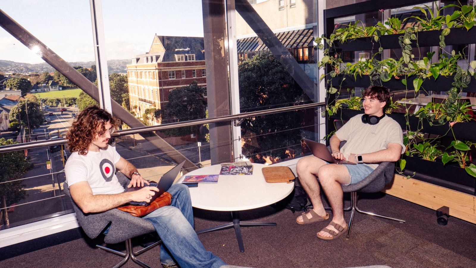 Two people using laptops in a bright indoor space with a round table and vertical garden.