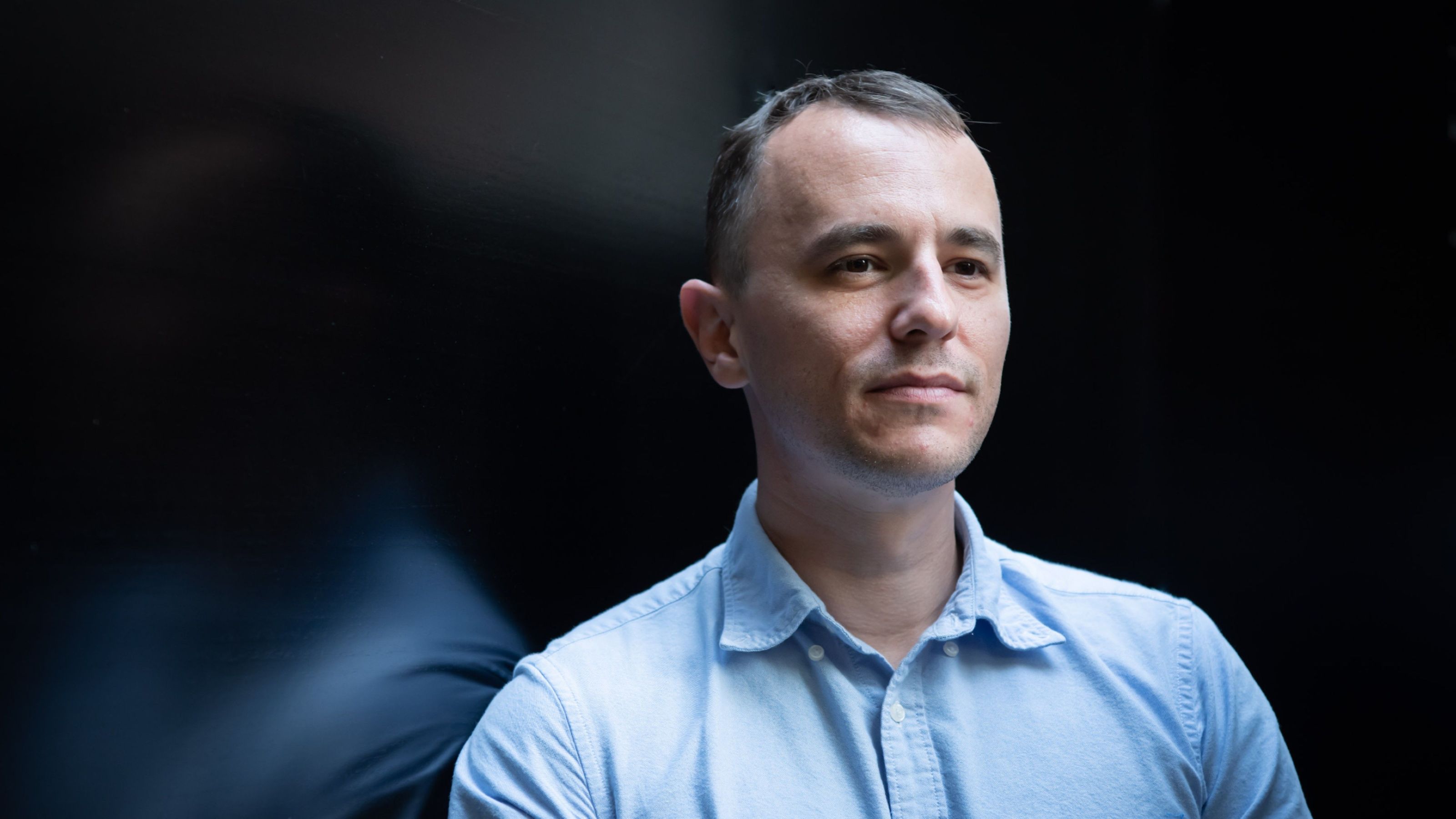 Dr Stephen Skalicky standing in front of a dark glass wall. 