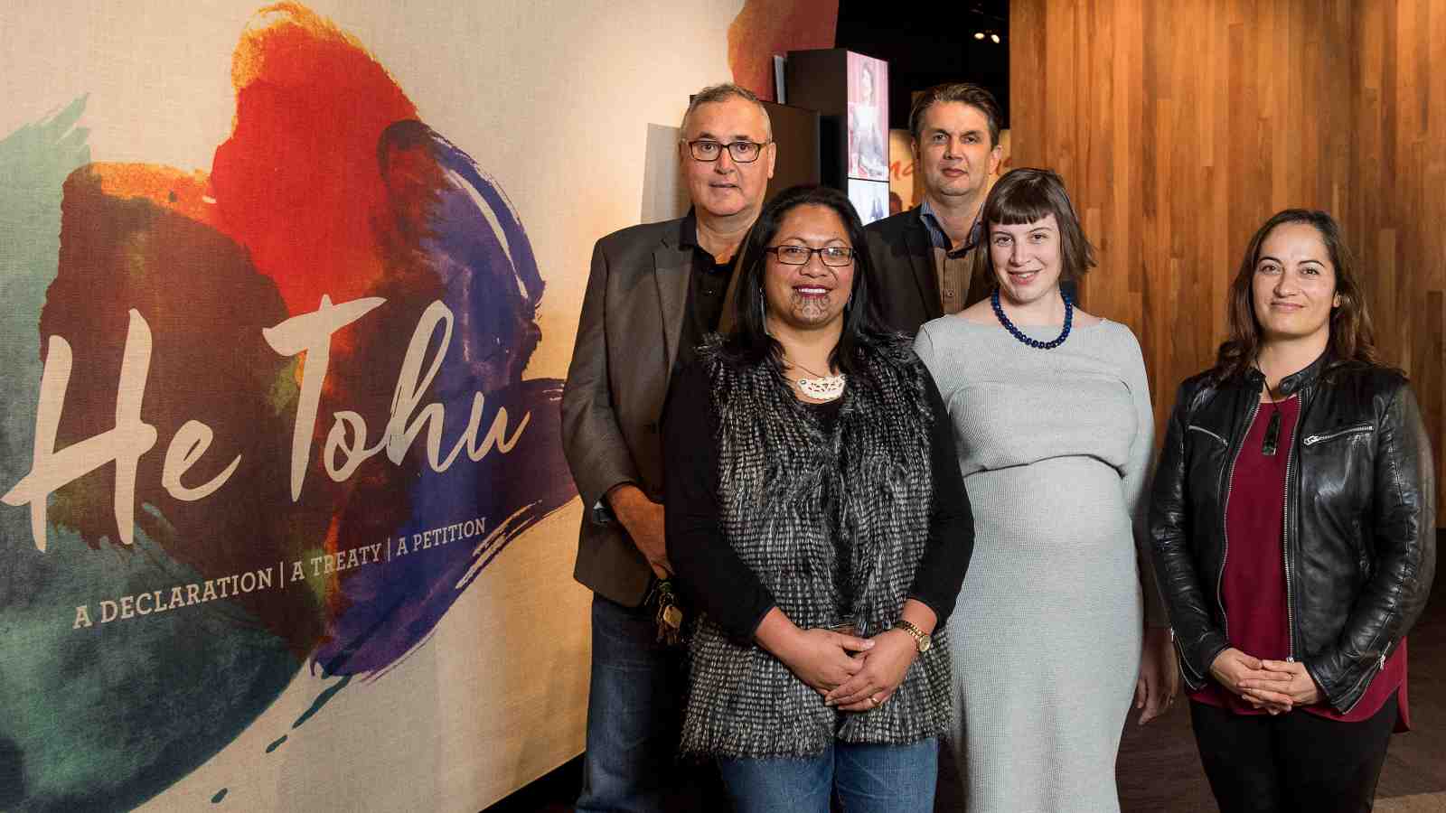 Victoria University staff stand in front of the He Tohu exhibition sign.