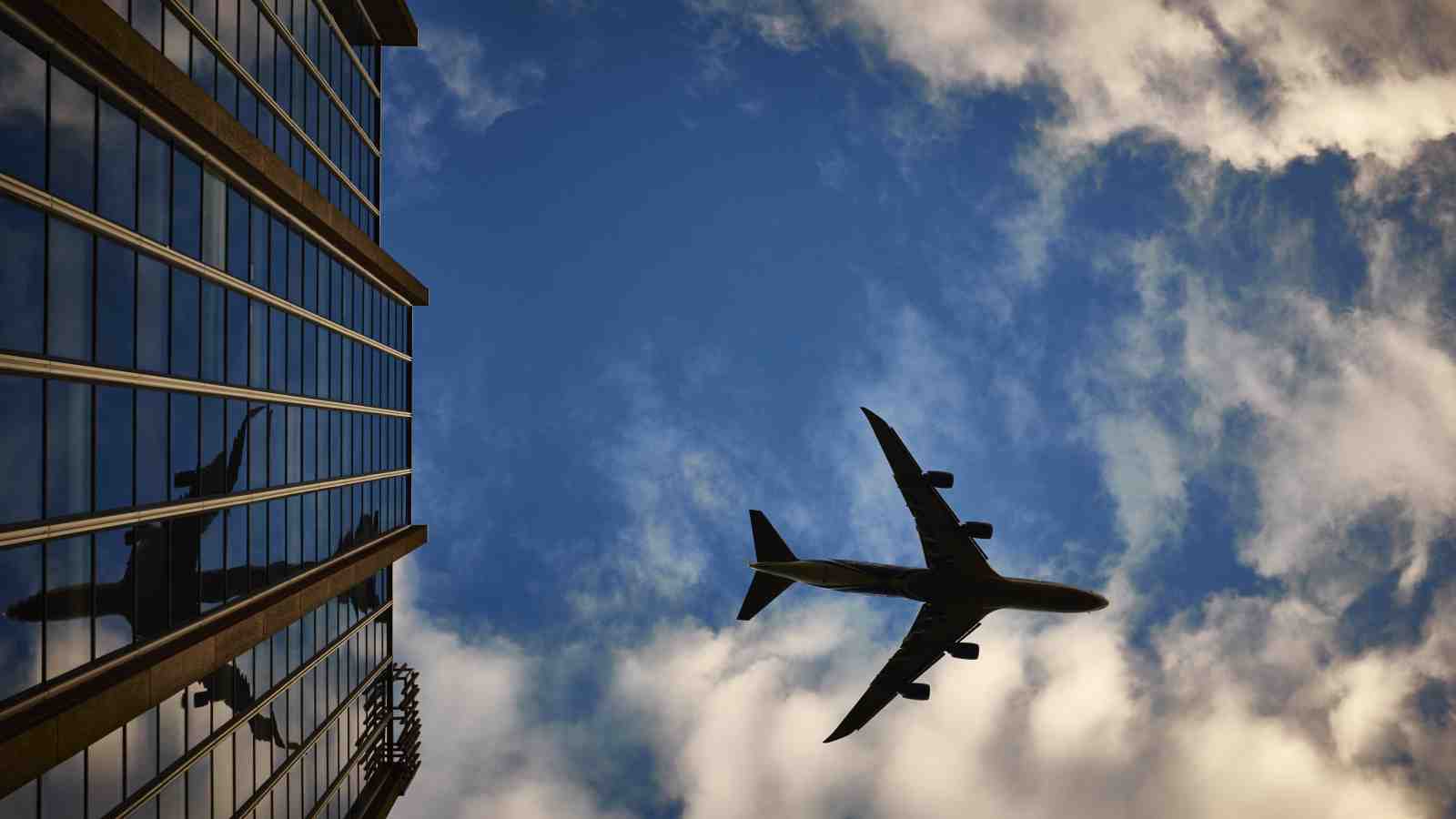 A plane high in a blue and cloudy sky, reflected in a sky scraper.