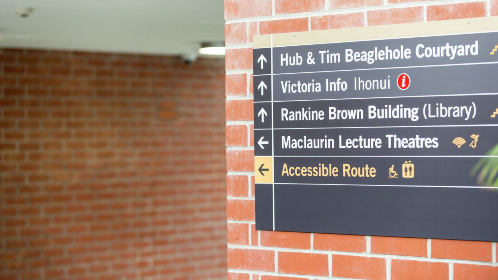 A black sign on a brick wall that shows where an accessible route is located.