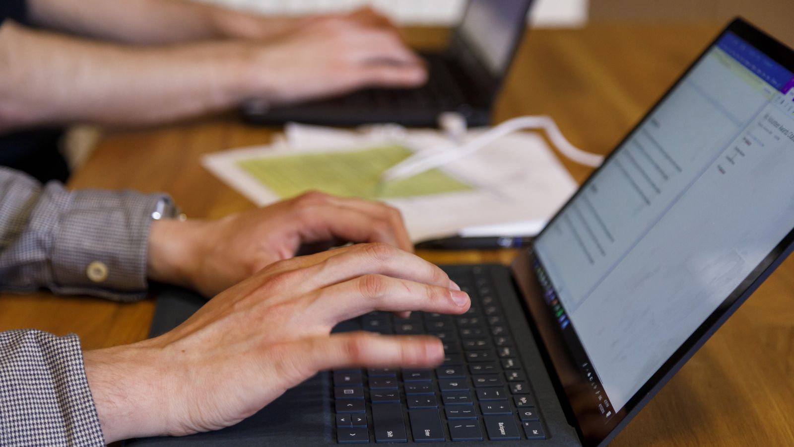 Two people's hands are typing on individual laptops.