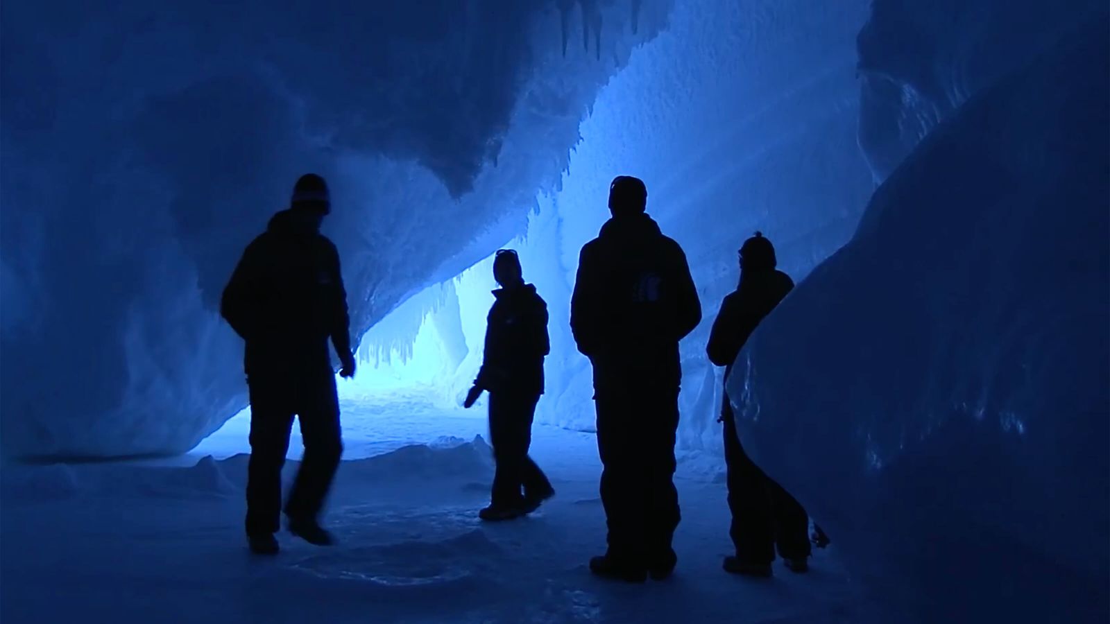 Human silhouettes explore an intensely blue ice cave.