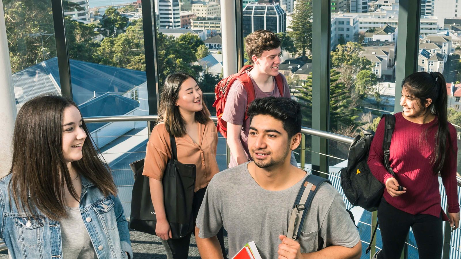 A group of students climb the stairwell in Rankine Brown, with a view of Wellington city out the windows behind them