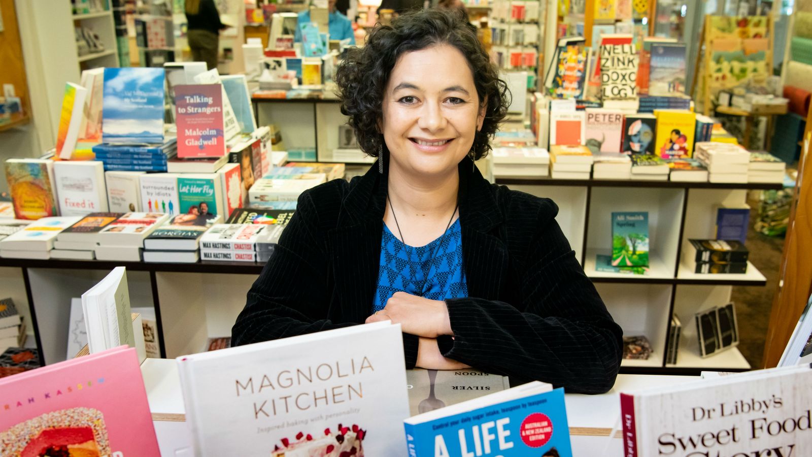 Lisa Te Morenga posing for a photo in a bookshop with books about sugar in the foreground.