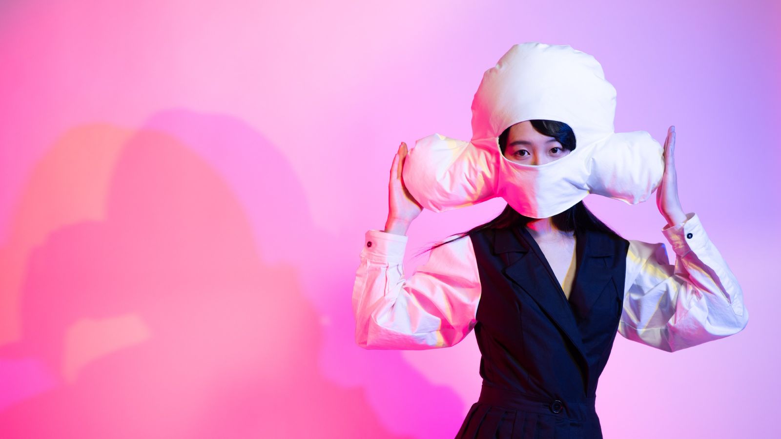 Model wearing cloud shaped head piece in front of pink background