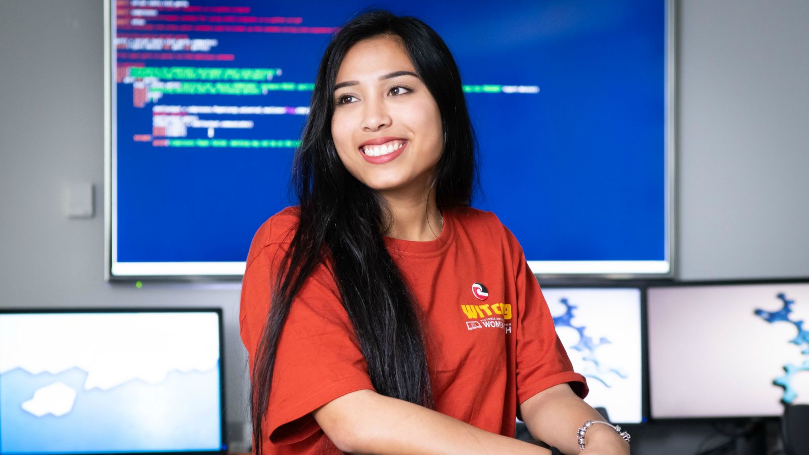 Smiling woman stands in front of screen of code.
