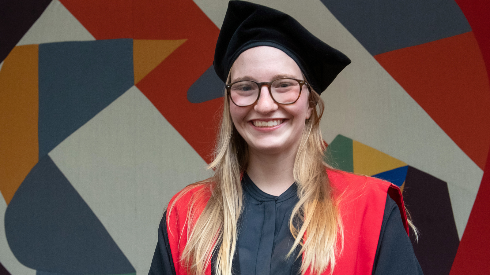 Girl with long blonde hair grinning, wearing a tricorn hat and doctoral robes