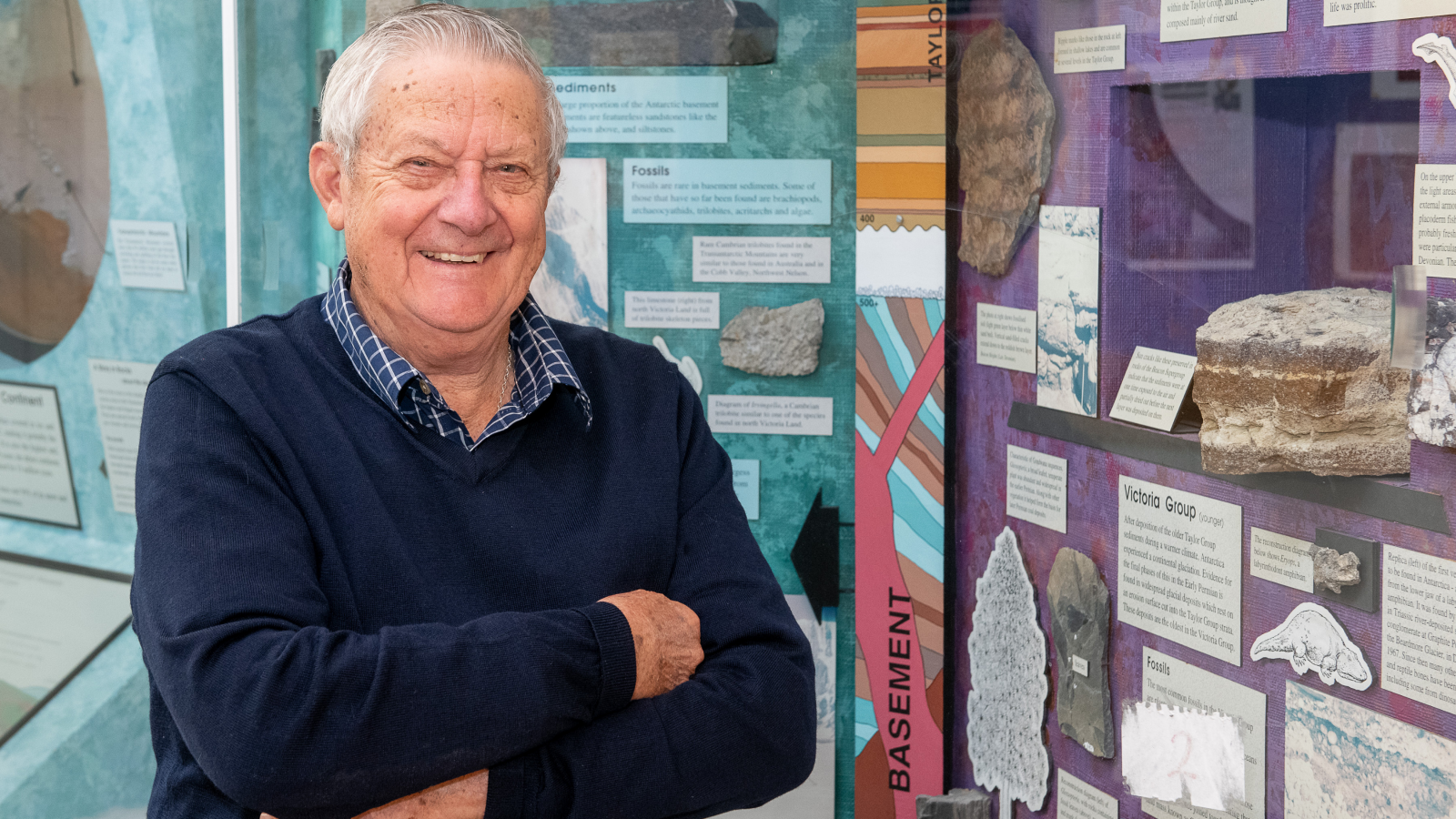 Old man with white hair in front of a display of rocks