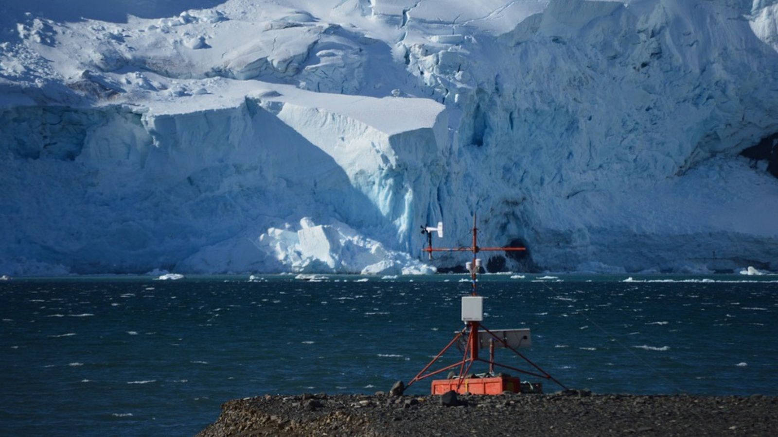 Orange spindly weather station with antarctic ice behind, in middle of ocean