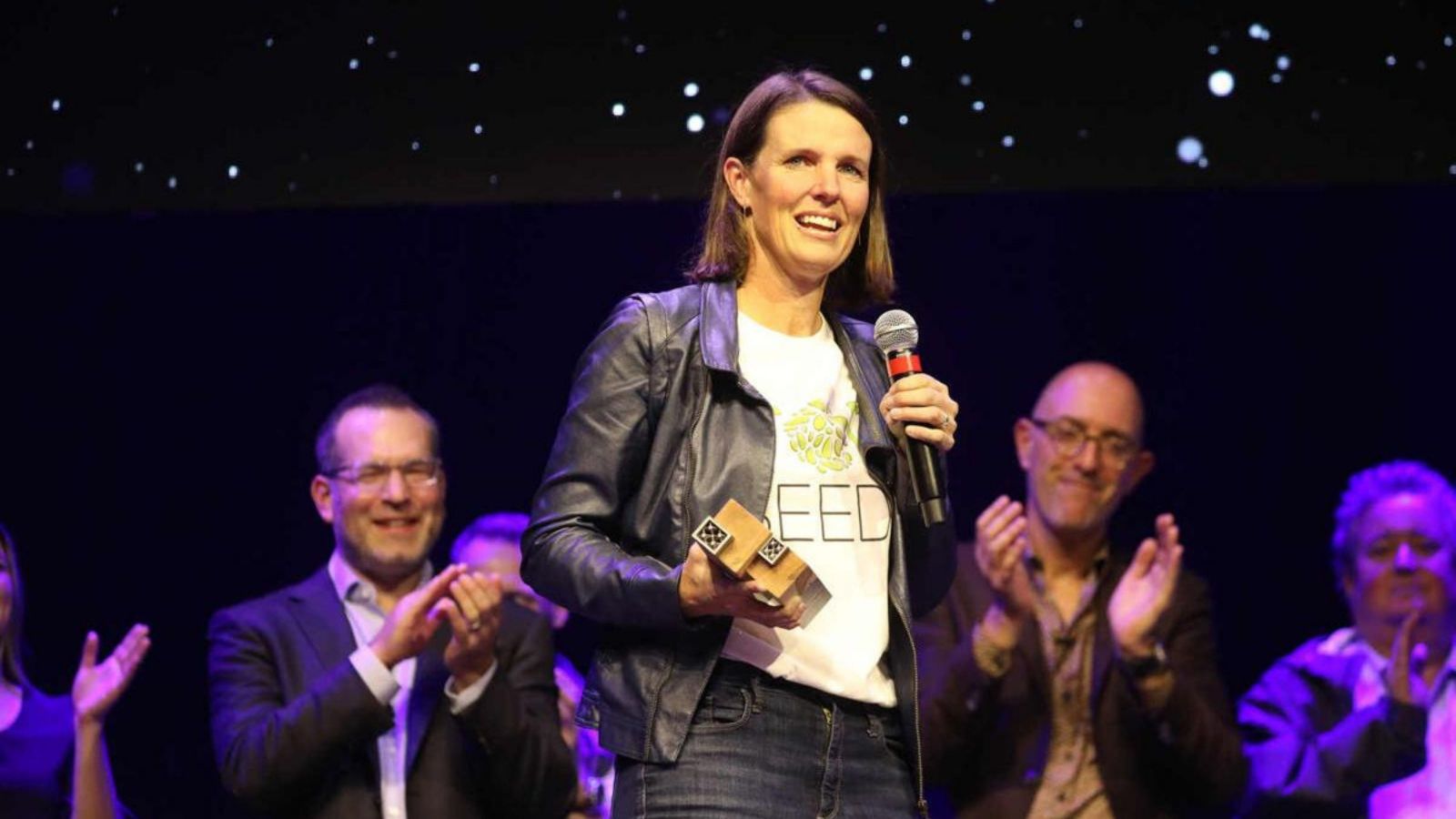 Girl with shoulder length hair holding award, wearing top with 'top seedz' on it