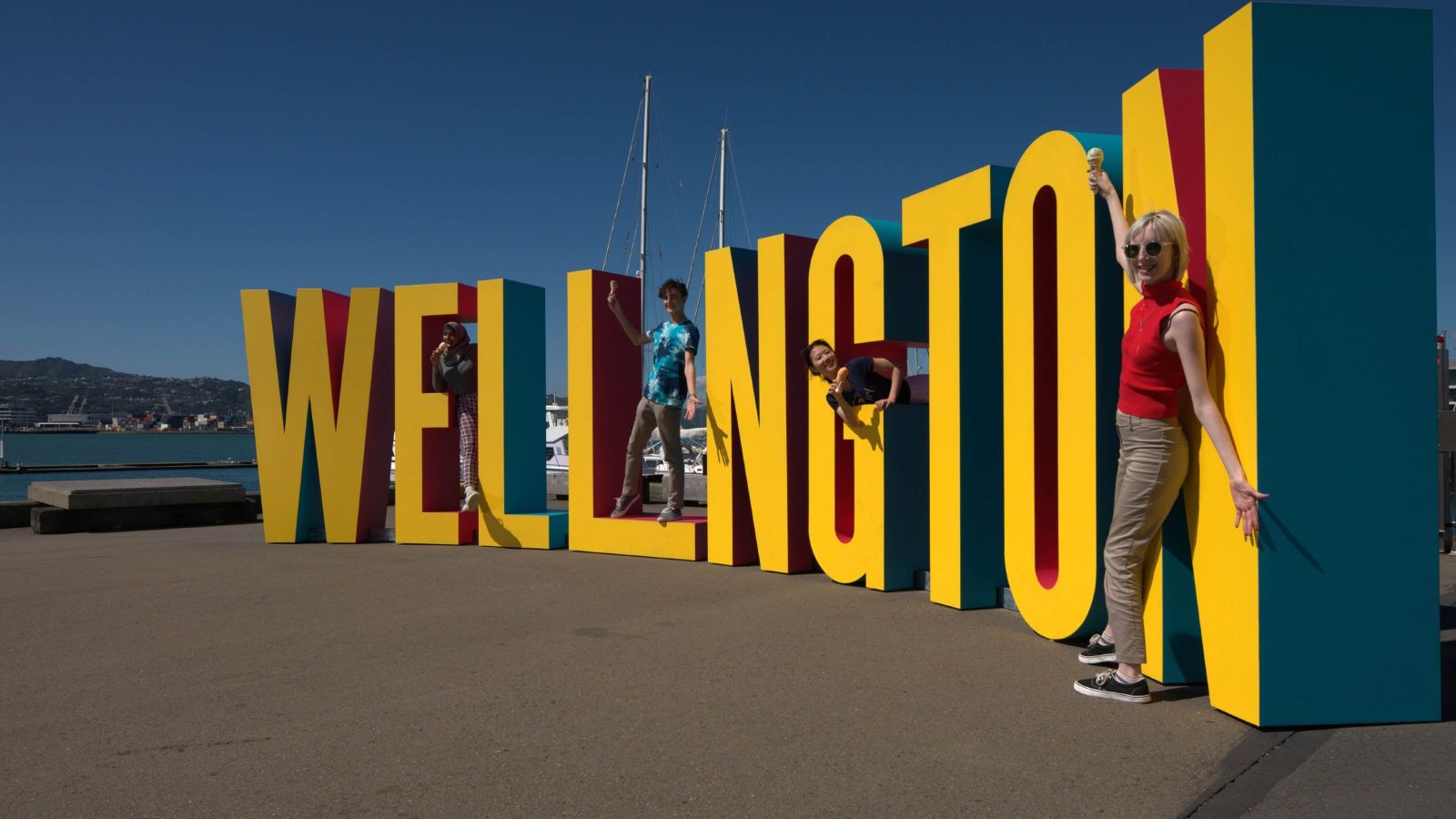 Students standing next to and on the yellow ‘Wellington’ sign on the waterfront.