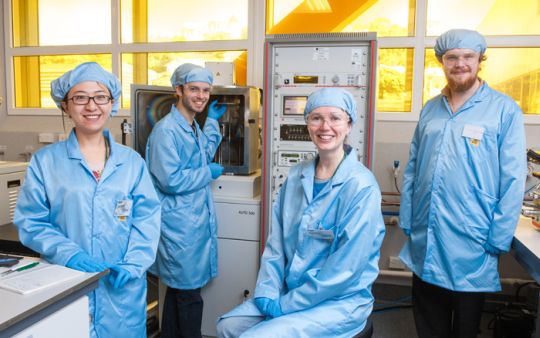 Four people wearing blue lab gear in a laboratory