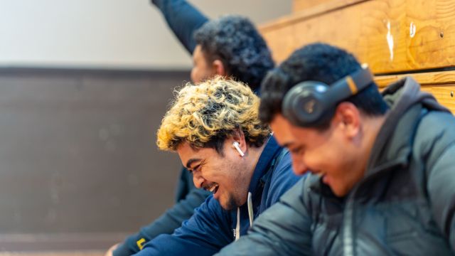 Three male Pasifika students sit on the benches in the Rec Centre, supporting a game.