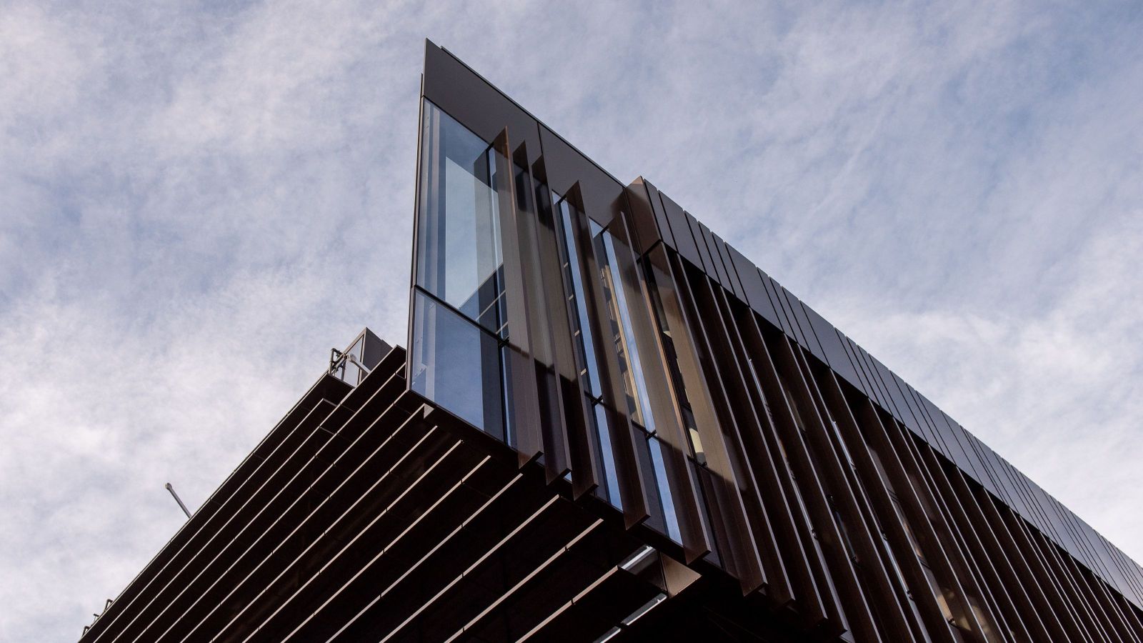 Close-up view of a modern building with angled glass and vertical metal fins against the sky.