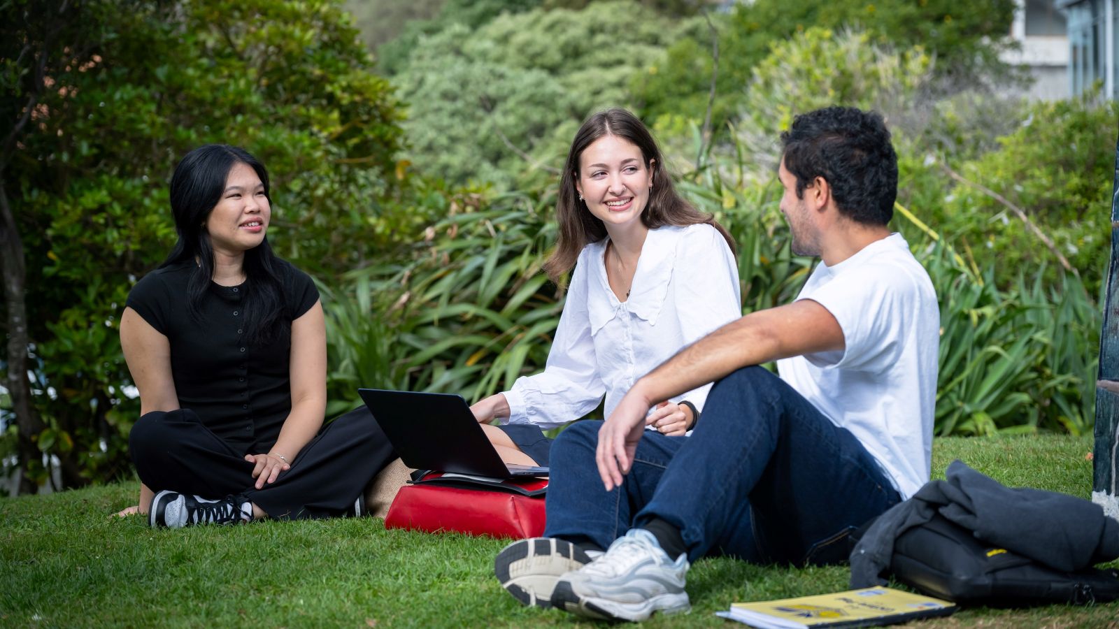 Three scholarship recipients are sitting on the grass are smiling on the Hunter building landing