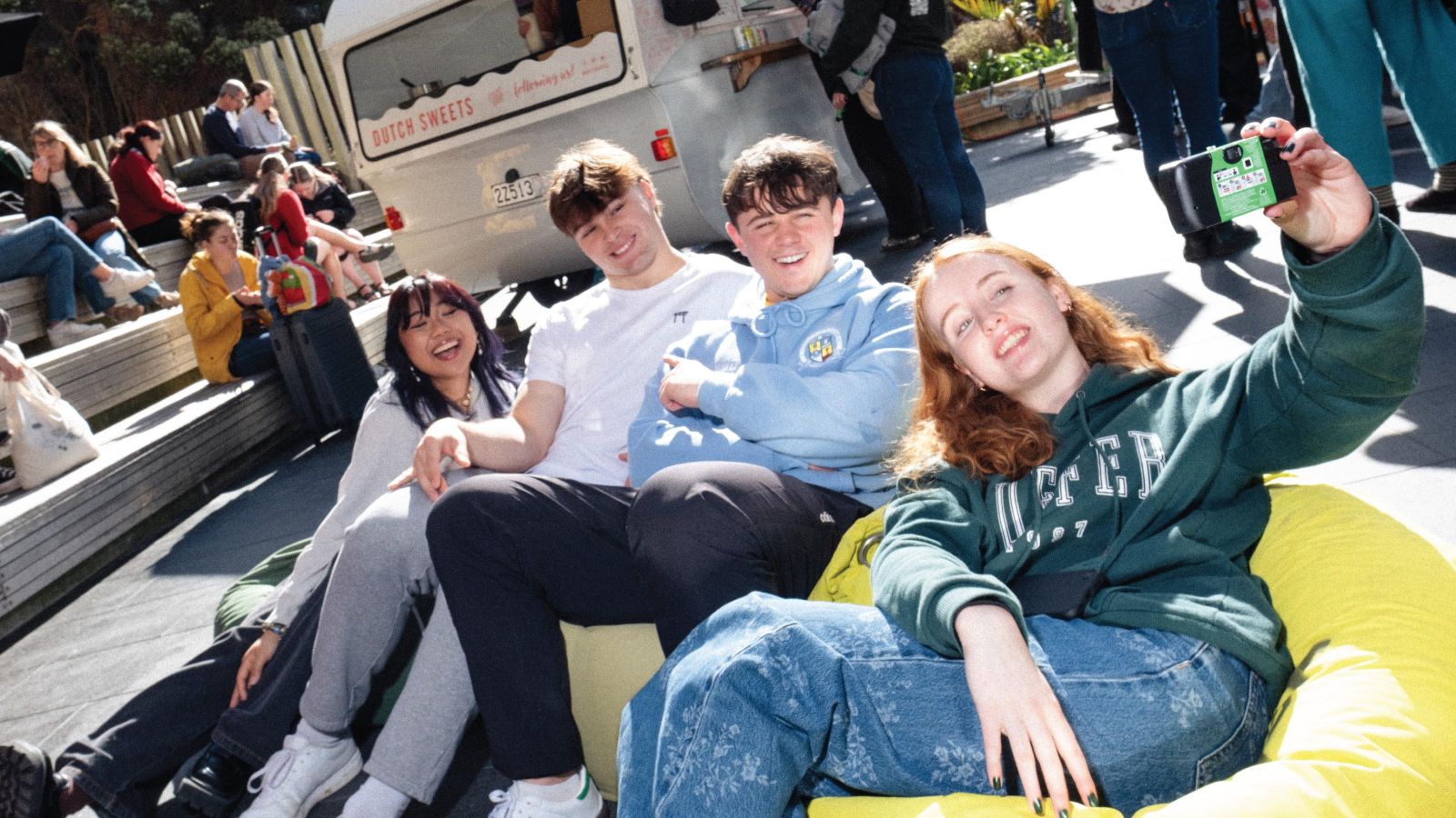4 students sitting on the ground on beanbags, taking a selfie with a disposable camera