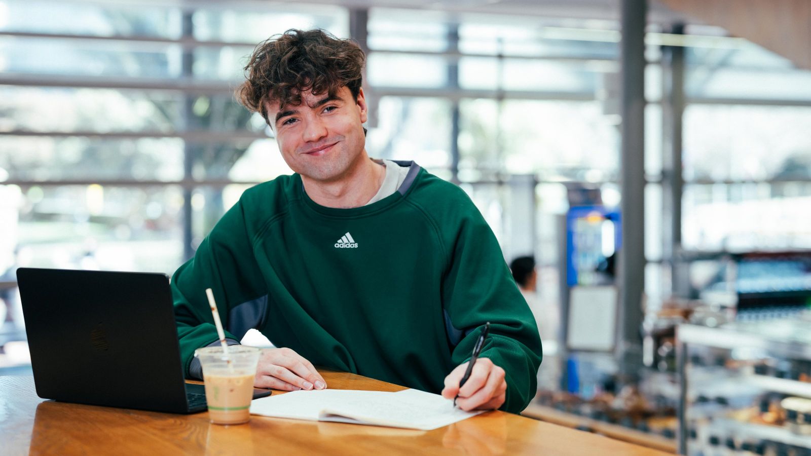 Male student at a desk with pen, paper, coffee and laptop.