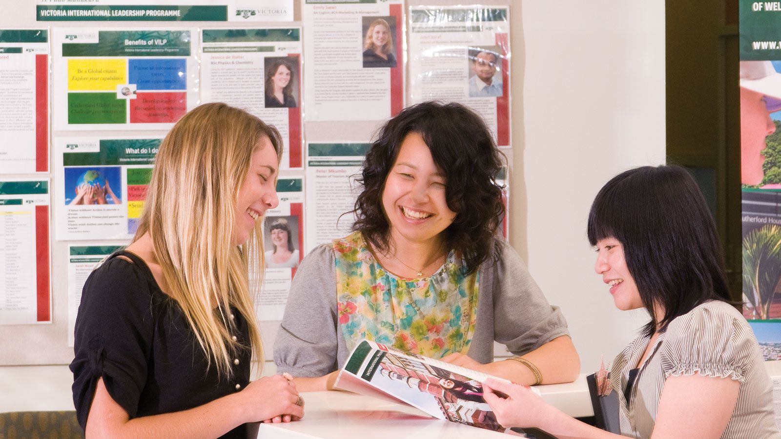 A female advisor and two female students smile while looking at pamphlet.