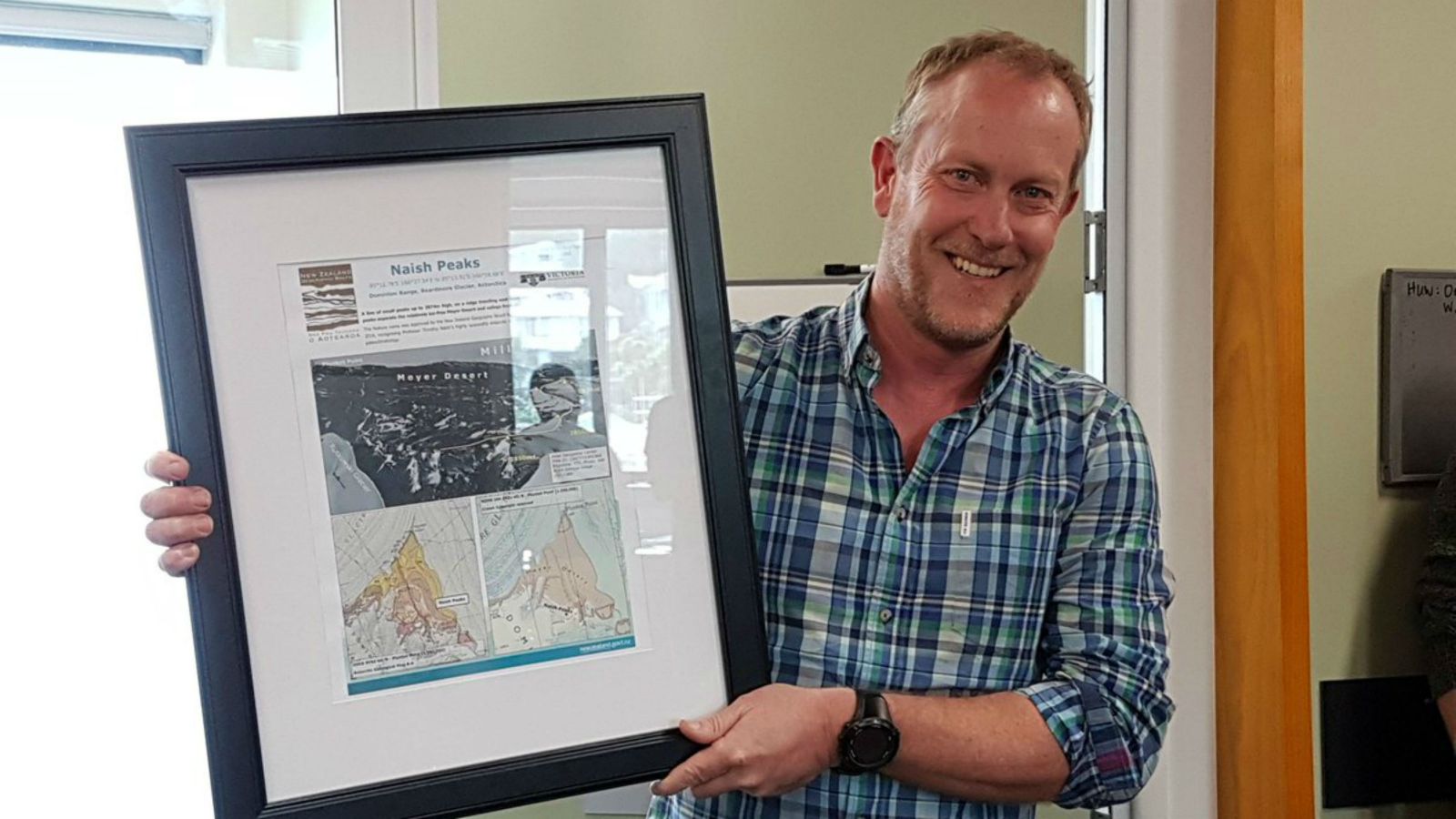 Professor Tim Naish holds framed image of Naish Peaks