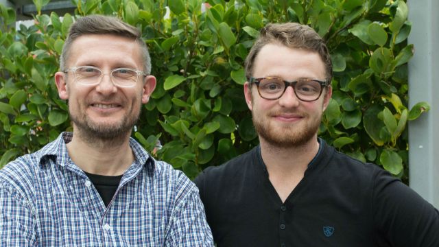 Lecturer Marco Sonzogni and postgraduate student Rory McKenzie stand in front of a leafy green backdrop.