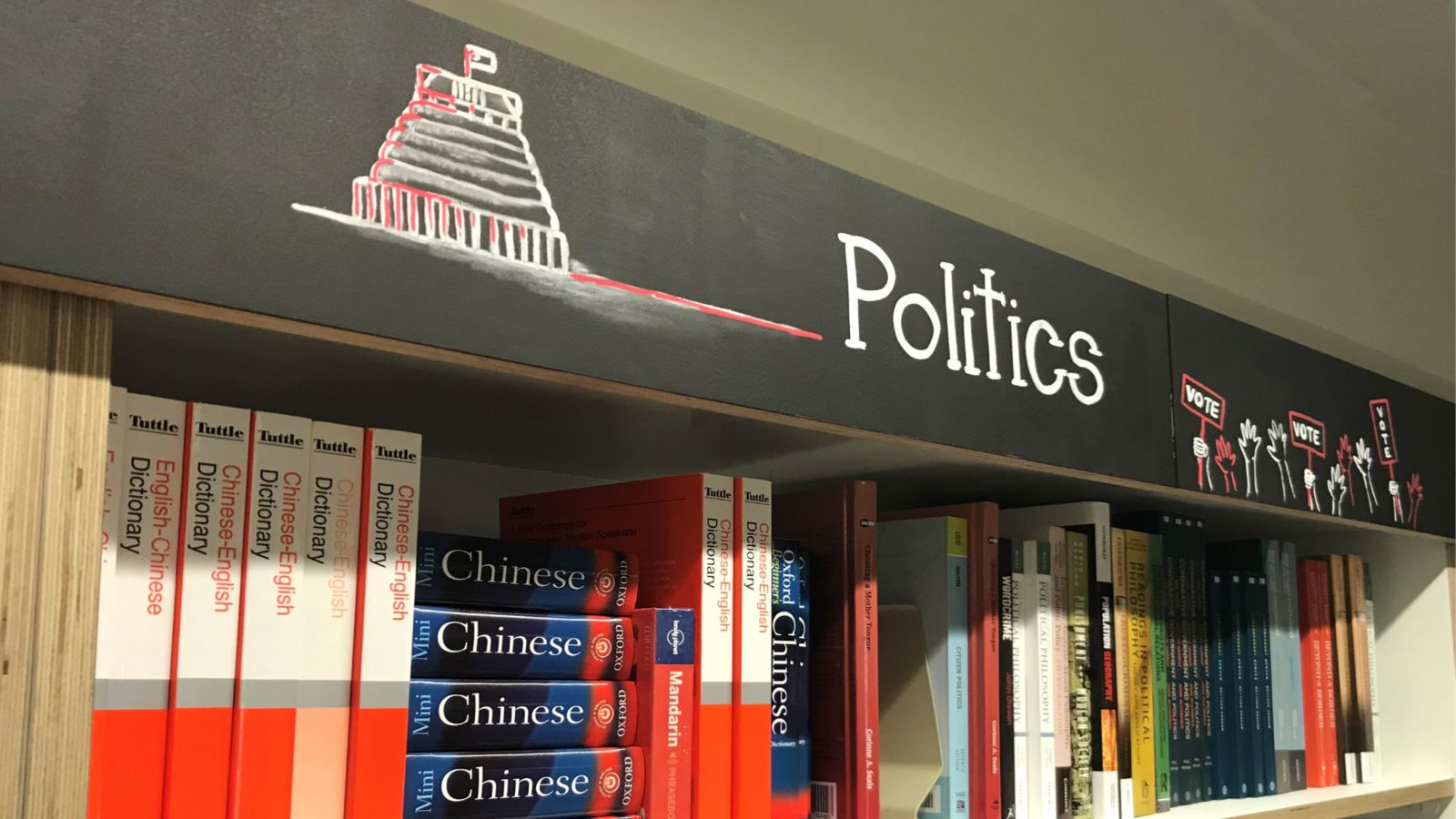 Bookshelf with Chinese—English dictionaries and various other books under a sign that says 'Politics'.