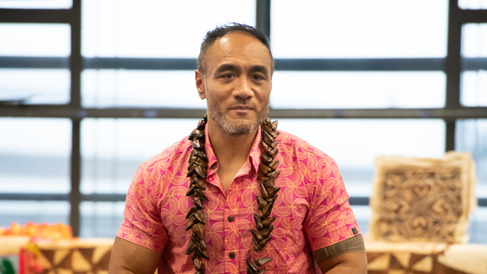 Samoan man wearing patterned pink samoan top looking past camera