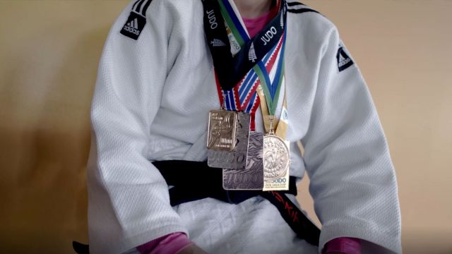 A close up of a person in a white martial arts uniform with medals around their neck