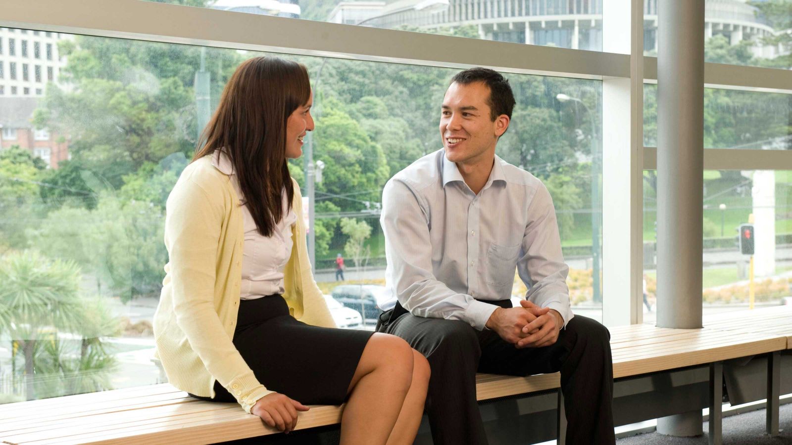 A man and woman are seated in discussion by a large window.