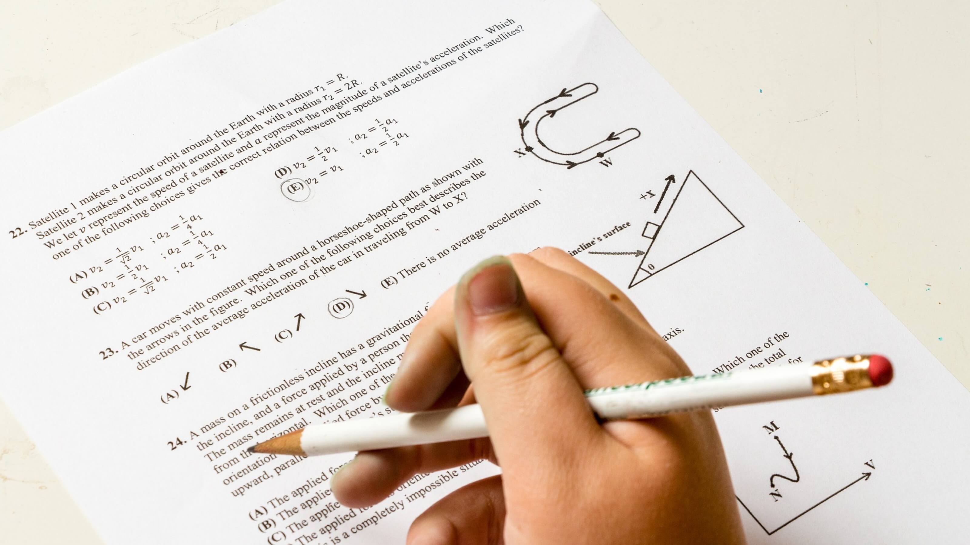 A close up of a hand holding a pencil filling in an exam paper.