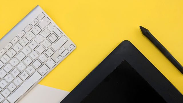 overhead view of mac keyboard, tablet and stylus on yellow background, 