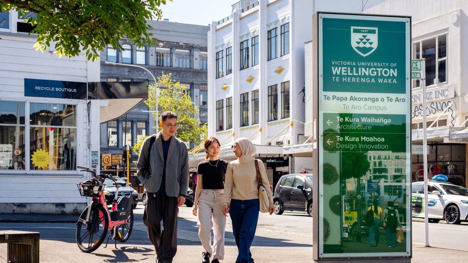 Three students walking on Te Aro Campus with city in background