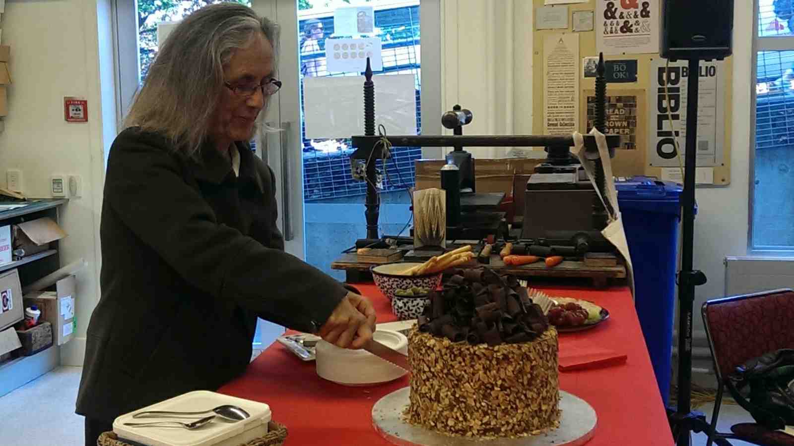 Author Patricia Grace cuts a very elaborate birthday cake topped with chocolate curls – at Wai-te-ata Press. Image credit: Meredith Paterson.