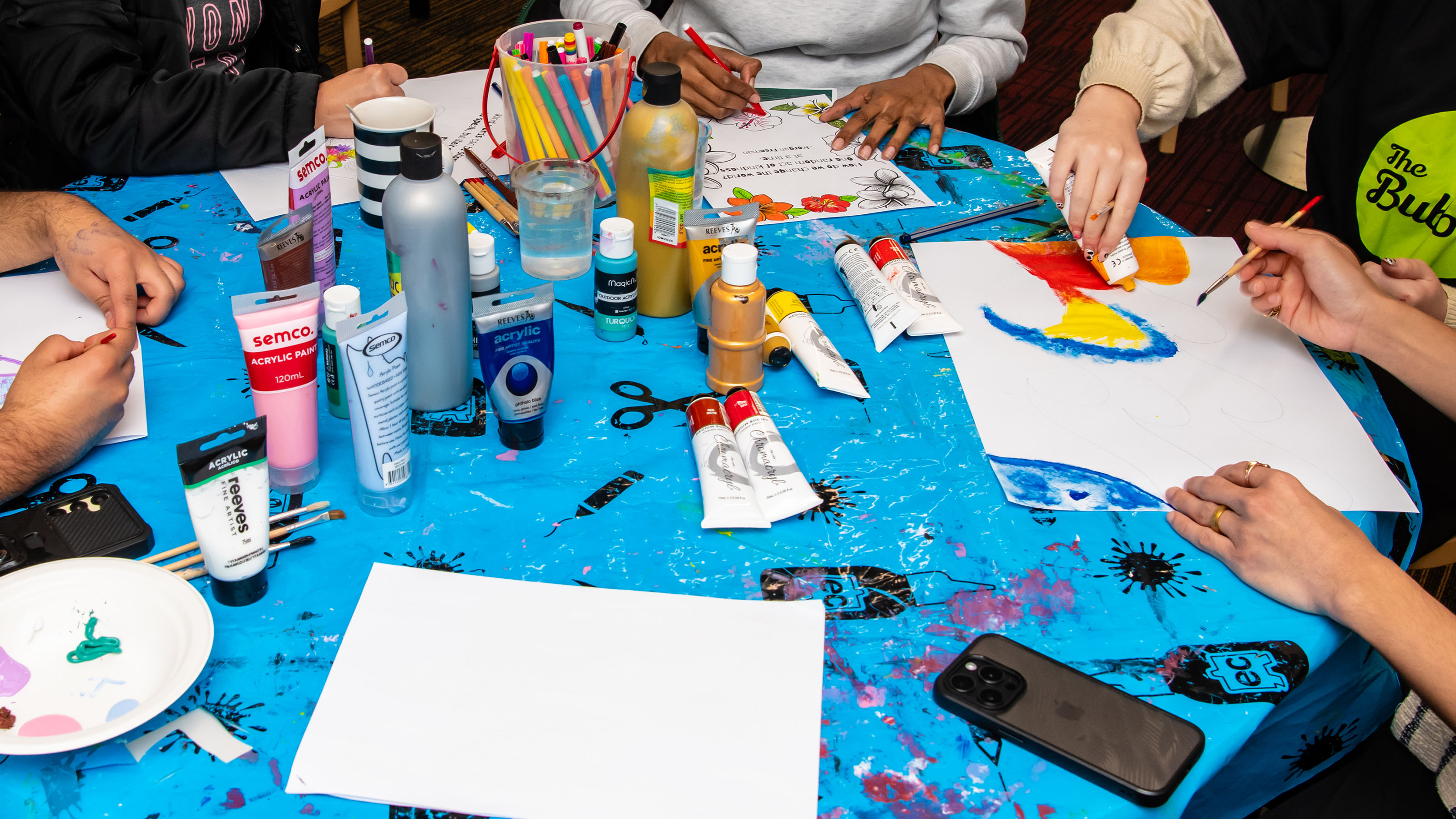 A photo showing busy hands painting on a blue table.