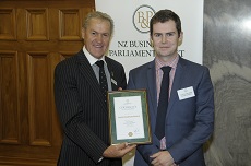 Caleb wearing a suit and standing with Rt Hon David Carter receiving his certificate. 