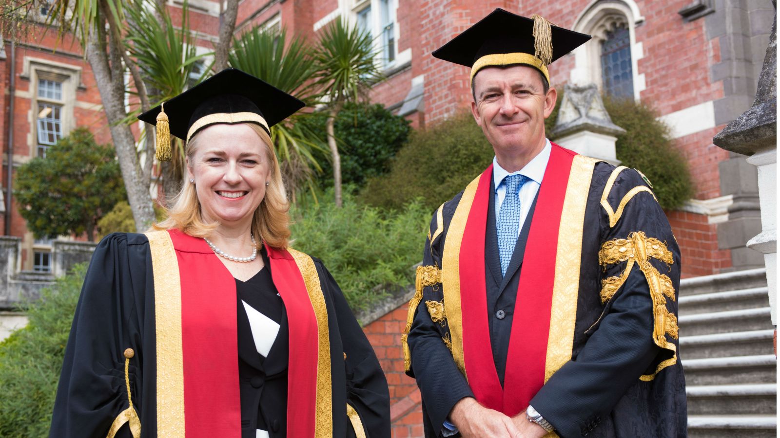 Chancellor Neil Paviour-Smith and Pro-Chancellor Dame Therese Walsh posing in academic dress before the Hunter building