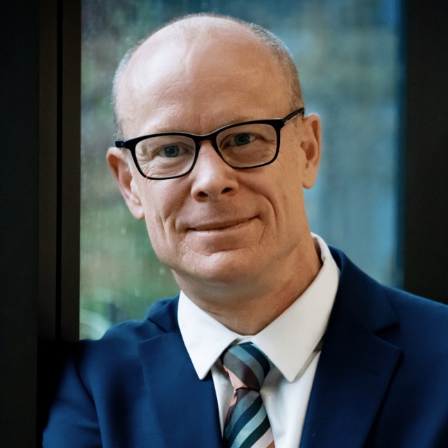 Vice-Chancellor Nic Smith wearing a suit in front of a dark window