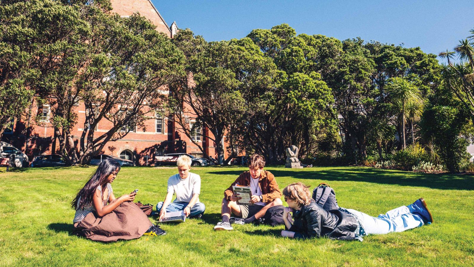 Four students relaxing on grass on a sunny day