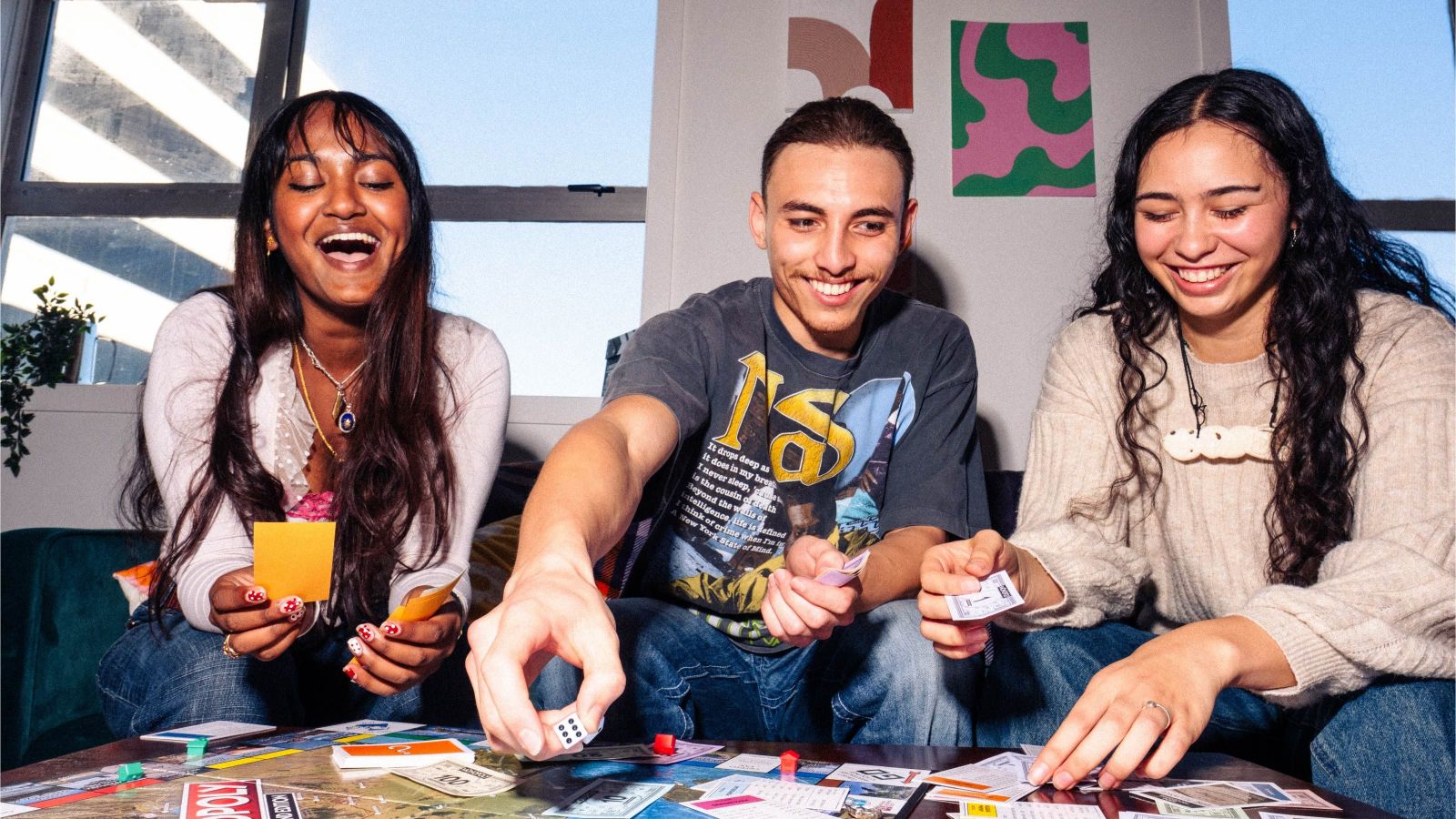three students laughing playing a board game with cards and dice