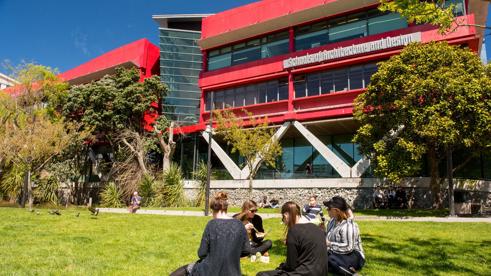 A group of students sit on the grass outside the red Te Aro campus building