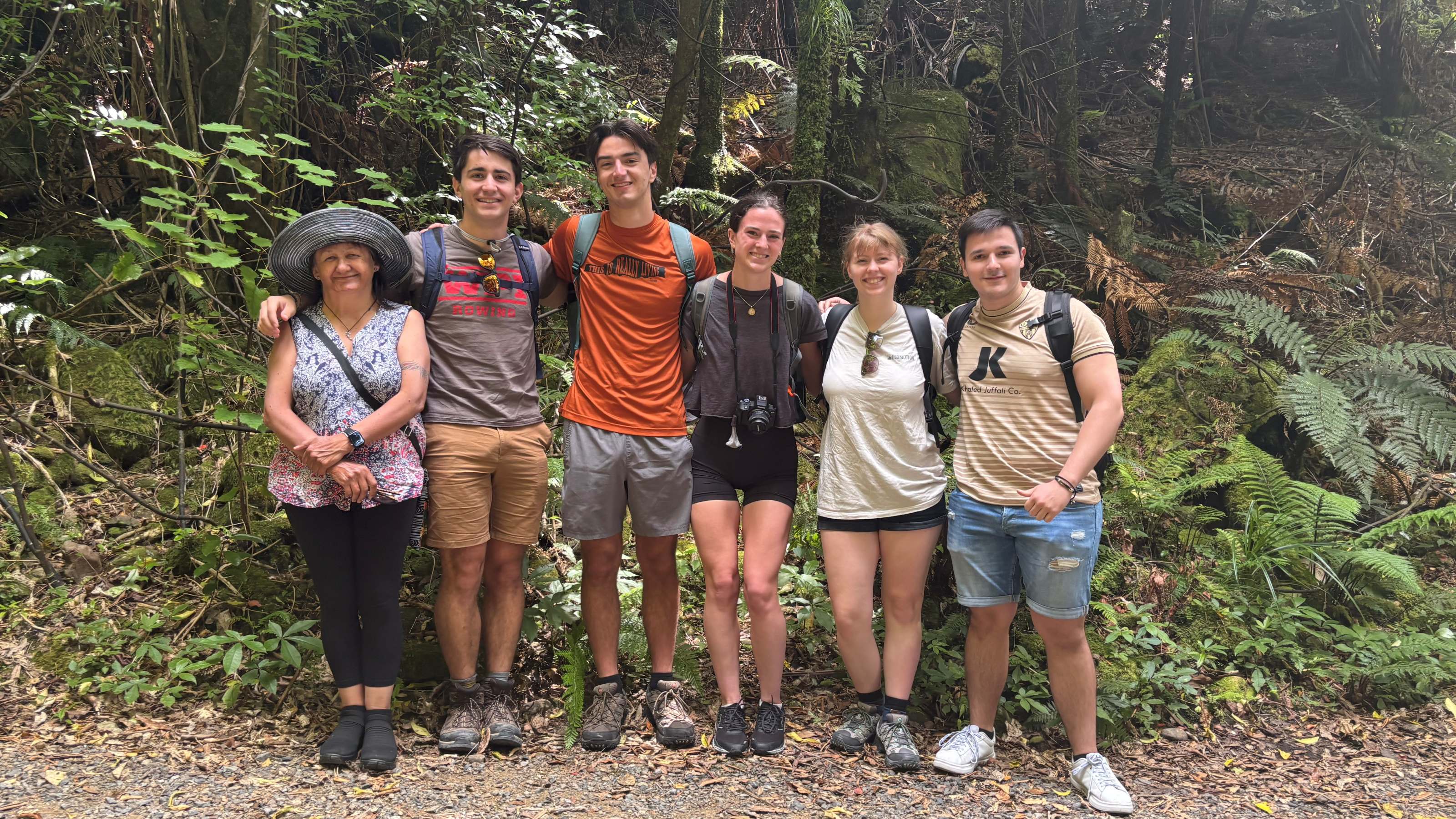 Group of people standing in a line with their arms around each other on a bush path with trees and bush in the background. 